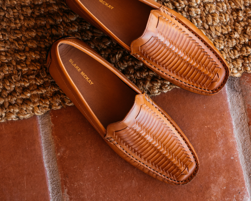 Top-down view of woven leather loafers by Blake McKay on a terracotta floor and textured rug—used in a subscribe section inviting users to sign up for exclusive deals, special offers, and upcoming events.
